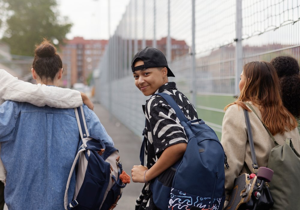 En vennegjeng som går forbi en fotballbane, hvor han ene ser seg tilbake mot kamera og resten ser rett frem