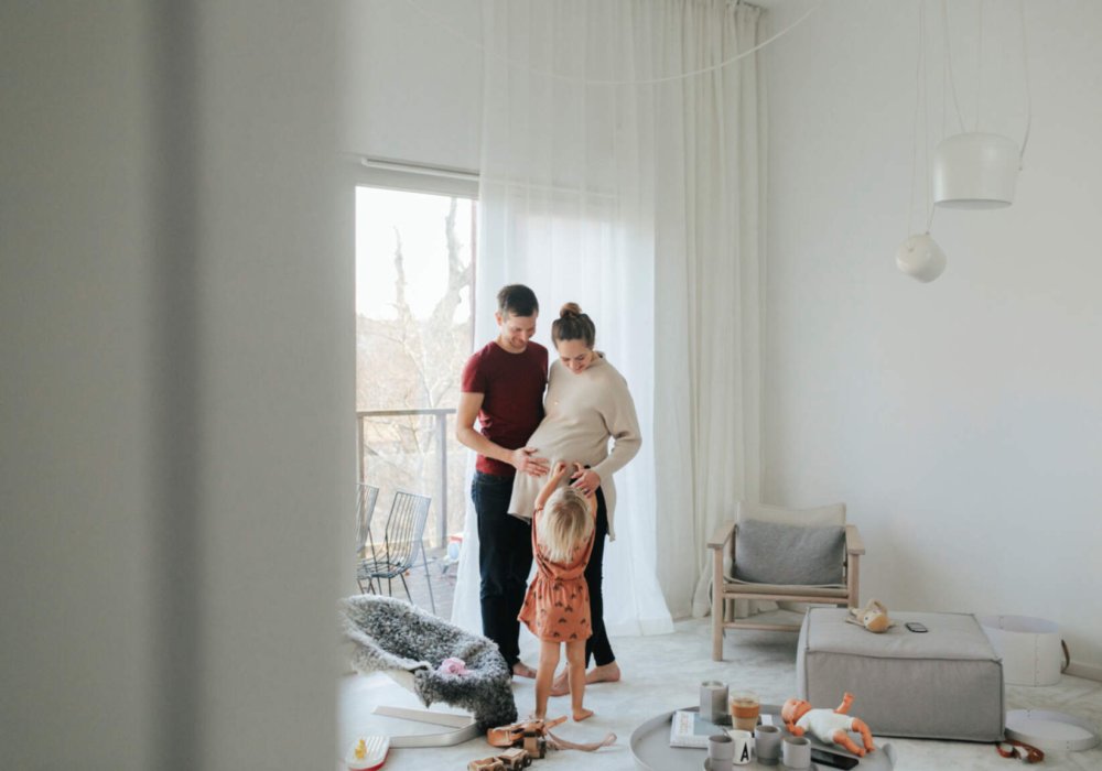 Gravid dame som står med familien sin i en stue.