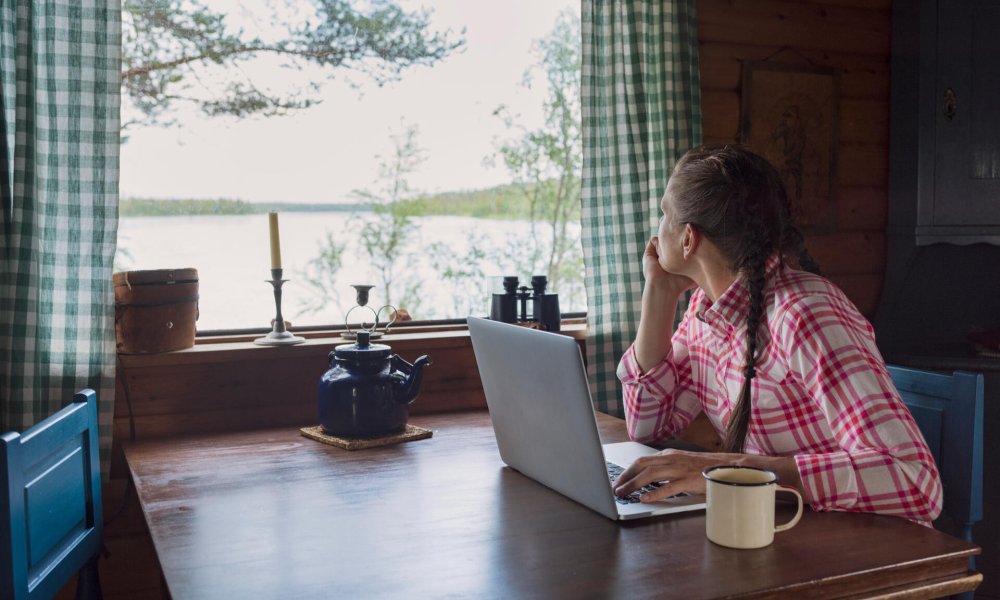 Illustrasjonsfoto: En kvinne sitter innendørs på en hytte med en pc.