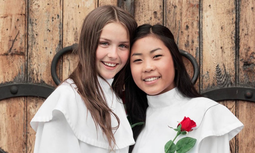 To smilende jenter i hvit konfirmasjonskjole