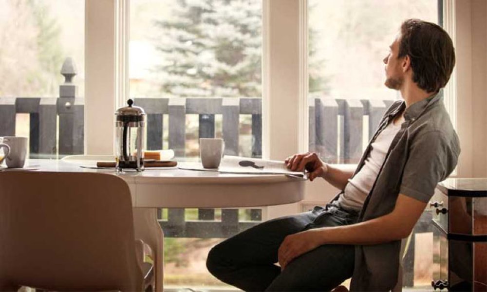 Mann ved frokostbord som ser ut av vinduet